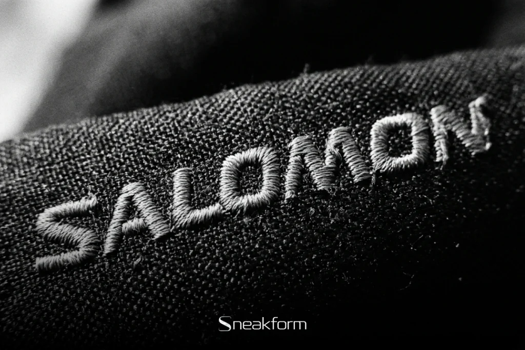 Broderie Salomon en gros plan sur textile noir, artisanat et identité technique de la marque.