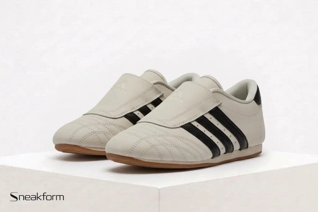 Sneakers tendance 2026, Adidas Taekwondo en cuir crème avec trois bandes noires et semelle gomme.