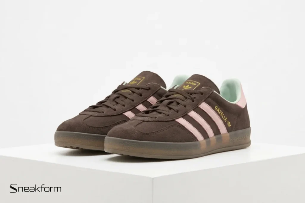 Sneakers tendance 2026, Adidas Gazelle Indoor en suède marron avec bandes roses et semelle gomme translucide.